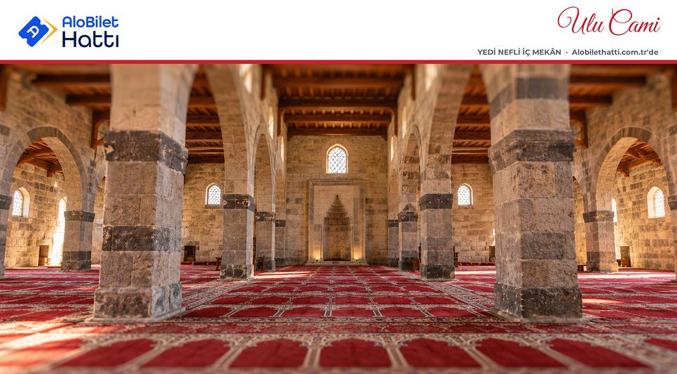 Kalın taş payeler arasında uzanan sade, alçak tavanlı cami iç mekânı